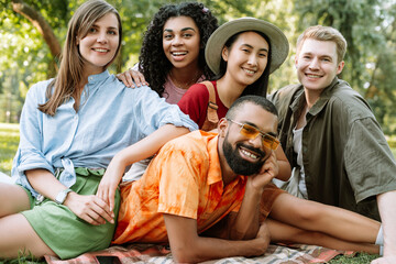 Wall Mural - Group of multiethnic, smiling friends having fun relaxing together in park posing and looking at camera