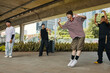© DragonImages - Group of young men breakdancing under urban bridge in North Seoul Park Brimming with energy, they exhibit skillful movements in shaded area with greenery background