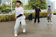 © DragonImages - Young man dancing enthusiastically in urban park surrounded by greenery and cityscape while two people observe and smile