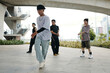 © DragonImages - Group of young Asian dancers performing under urban bridge with focused expressions On concrete pavement, they move in unison while practicing their dynamic dance routine