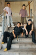 © DragonImages - Group of four young friends standing and seated on staircase under urban structure showing casual style and streetwear fashion