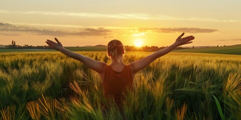 Woman with arms outstretched standing in a vibrant wheat field, basking in the warm glow of sunset, symbolizing freedom, joy, and the beauty of nature.