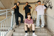 © DragonImages - Group of four young people hanging out on stairwell under graffiti-covered bridge, smiling and making peace signs, capturing urban lifestyle and casual gathering
