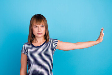 Photo of serious woman raise arm palm empty space stop gesture isolated on blue background