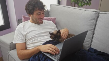 Sticker - A young hispanic man wearing a white shirt is having a video call with a laptop while sitting on a grey sofa in a living room with a cat on his lap.