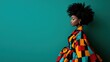 ©  lukaPixMedia - A stylish woman with an afro hairstyle, wearing a colorful, patterned outfit, standing against a green background. The image is striking, fashionable, and well-composed.