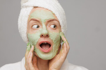 Joyful emotional woman applying green mask on face, facial skin care concept, cosmetology