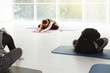 © ninelutsk - Yoga teacher demonstrates pose as students follow along in light studio. Group practice on morning session with mid aged woman class