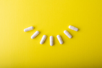 White pills isolated on yellow background. Vitamin C supplement capsules. White vitamins capsule. Treatment and prevention of flu and colds. Healthcare concept banner. High quality photo