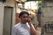 © Mdv Edwards - A young asian man having a serious conversation on his cellphone. Negotiating terms. Slum area background.