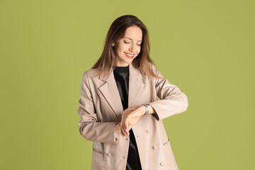 Canvas Print - Beautiful woman in stylish beige jacket checking time on olive background