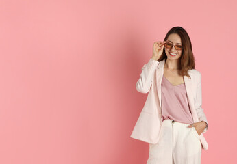 Poster - Beautiful woman in stylish white suit and sunglasses on pink background, space for text