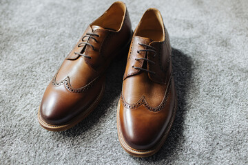 Brown leather shoes. Groom getting ready for the wedding. Wearing clothes dressing up. Man fashion background. Gray fluffy carpet clothing detail. Footwear object isolated on floor.