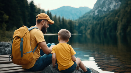 Sticker - A bearded man and a young boy, both wearing yellow outfits, sit by a tranquil lake surrounded by a forest and mountains. The man has a yellow backpack.