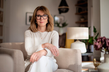 Wall Mural - Portrait of a mature woman wearing white sweater and pants and sitting in her modern home