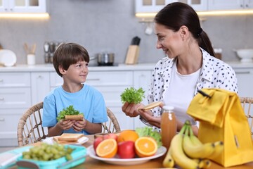 Poster - Mother and her cute son preparing lunch box with healthy food at wooden table in kitchen