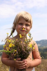 Canvas Print - Smiling little girl with bouquet of wildflowers at field