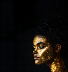 beautiful young woman, face covered golden paint; close-up of artistic feminine head; short hairs; idea of beauty, nature, mask, luxury cosmetics, art, feminism, make-up; black background; copy space