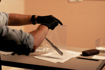 close-up detective's office middle-aged investigator in shirt and tie sitting desk examining evidence bloody knife murder weapon