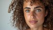 © Tatiana - Close-up of young woman's face with curly black hair on plain neutral background. Concept of improving hair appearance, revealing femininity and attractiveness, developing hairdressing business