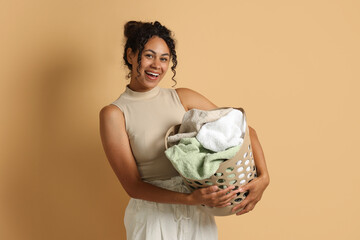 Poster - Happy woman with basket full of laundry on beige background