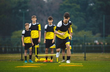 Wall Mural - Youth Football Player Running on Training Drill. Teenagers in Soccer Training Sportswear Exercising Outdoor. Sports Educational Equipment. Junior Football Club Practice Session