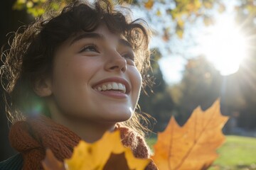 Wall Mural - A pretty girl in a black dress standing in an autumn park keeps the leaves close to her face