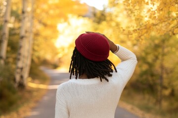 Wall Mural - Mid-adult hispanic woman wearing a hat during golden hour during autumn season with beautiful trees as a background.