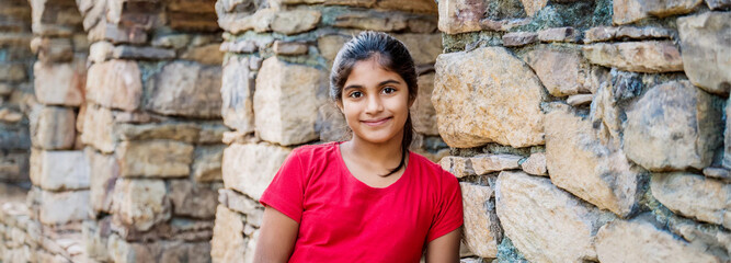 Wall Mural - A portrait of a South Asian girl smiling with her back against a stone wall.