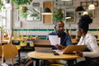 © Oleksii Syrotkin/Stocksy - Young waitress and black male cafe owner checking payments and bills