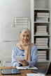 © Kritdanai - Confident Muslim Businesswoman: A young Muslim businesswoman in hijab smiles confidently while working in her modern office, showcasing diversity and success in the workplace.