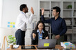 © Kritdanai - High Five for Success:  A diverse team of professionals celebrates a shared achievement with high fives in a modern office setting. The image exudes positive energy, teamwork, and a collaborative work