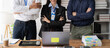 © Kritdanai - Confident and Ready: A diverse team of professionals stand united in front of a laptop, exuding confidence and readiness for the next challenge.  Their arms crossed, they project an aura of determinat