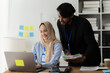 © Kritdanai - Collaborative Teamwork: A smiling woman in a hijab and a man work together on a laptop in a modern office setting, demonstrating effective communication and a supportive team dynamic.