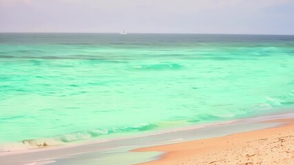 Poster - Capturing turquoise ocean waves gently crashing on a sandy beach with a sailboat sailing on the distant horizon