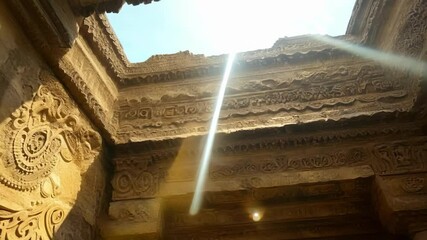 Poster - Rays of light are bursting through a hole in the intricately carved ceiling of an ancient stone temple, creating a mystical and ethereal atmosphere