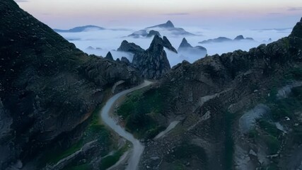 Aufkleber - Winding road leads to a mysterious cave in a foggy valley surrounded by mountains. The landscape feels adventurous and fantasy like, with cliffs and rocky formations adding to the wilderness vibe