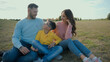 © Yuliia - Cute Caucasian happy family portrait joyful man male dad smiling woman female mom little boy child kid son sitting together hug embrace looking camera outside nature field farmland park picnic nature