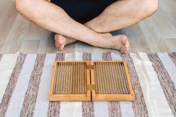 Man exercising yoga meditating sitting hands joined on the floor near sadhu board