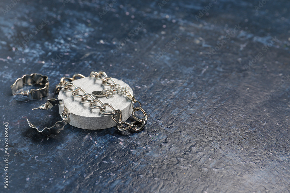 Decorative podium with silver earrings and necklace on grunge blue background
