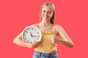 Canvas Print - Young woman with clock showing thumb-up on red background. Deadline concept