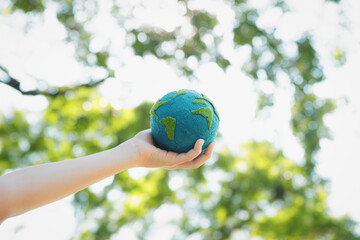 Young boy's hand holding planet Earth globe at natural park background as Earth day to save this planet with ESG principle and environment friendly energy for brighter future. Gyre