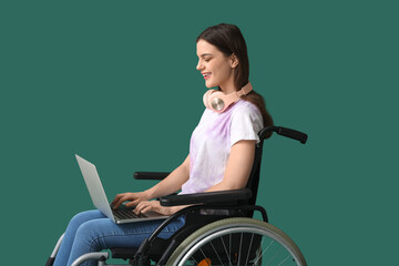 Wall Mural - Young woman in wheelchair using laptop on green background