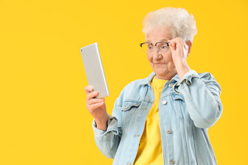 Poster - Senior woman in eyeglasses using tablet computer on yellow background