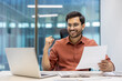 © Liubomir - Confident businessman celebrates success at modern office desk with laptop and documents in hand, feeling accomplished during workday
