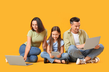 Wall Mural - Happy family sitting on floor with gadgets against yellow background