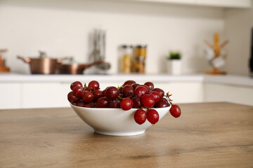 Bowl with fresh red grapes on wooden table in modern kitchen