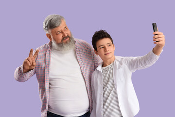 Wall Mural - Happy grandfather with his cute grandson taking selfie on purple background