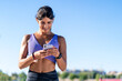 © Nibuya Qubik/Stocksy - A woman in athletic wear smiles while looking at her smartphone