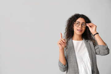 Wall Mural - Young African-American businesswoman pointing at something on grey background